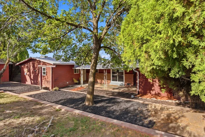 Red siding exterior with a covered porch, established trees, and dark landscape rock