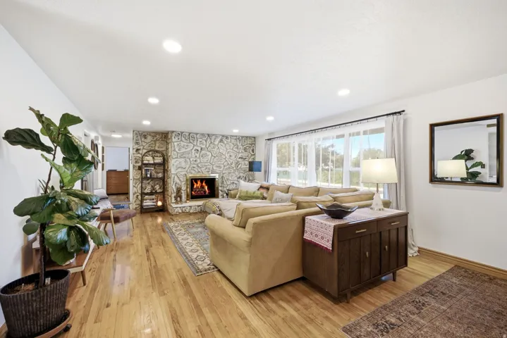 Hardwood flooring, stone accent wall with fireplace, recessed lighting, and large windows