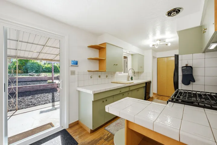 Kitchen featuring light green cabinetry, tile countertops, and wood-finish flooring