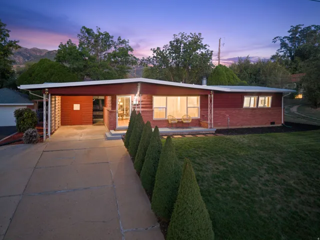 Mid-century modern exterior featuring a carport, brick and horizontal siding, mature front landscaping, and a manicured lawn