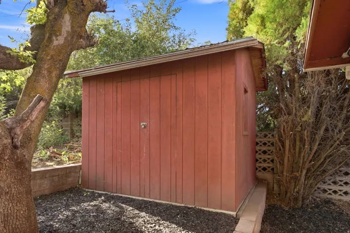 Red-painted utility shed with vertical wood siding and a single window