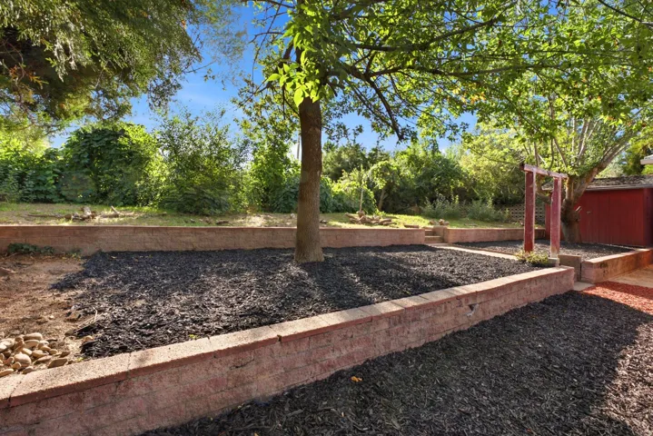 Tiered landscaping featuring brick retaining walls, established trees, and mulched garden beds