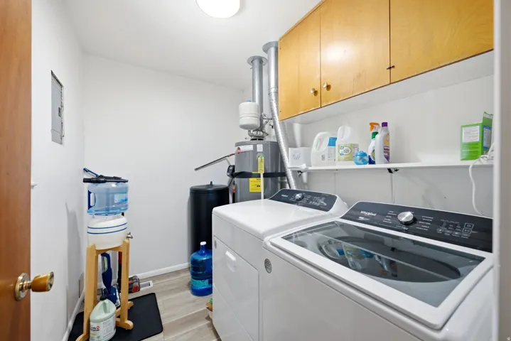 Dedicated utility area featuring wood-finish flooring, overhead cabinetry, and an integrated shelf for storage