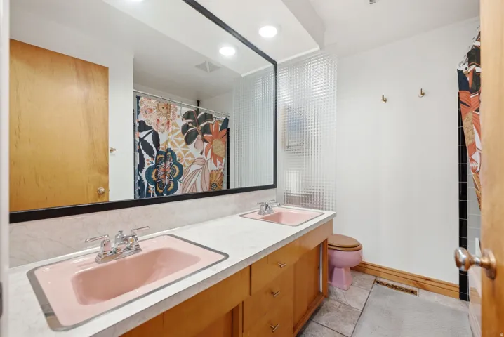 Double vanity with pink sinks, a large mirror, wood-finish cabinetry, and a textured glass divider