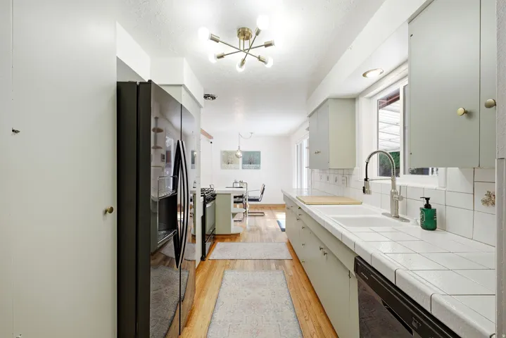 Galley kitchen featuring light wood-finish flooring, white tiled countertops, and a stainless-steel sink with a gooseneck faucet