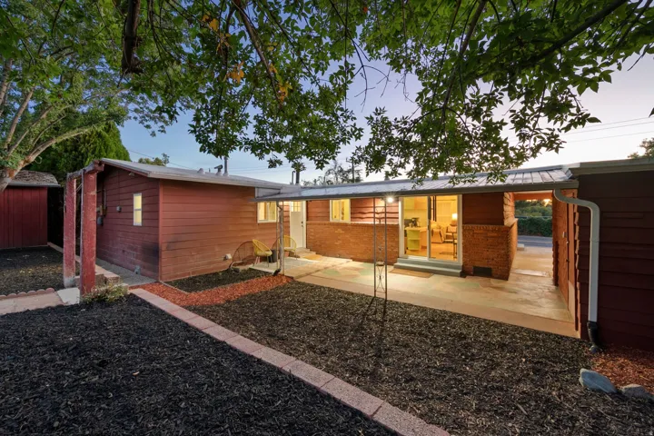 Exterior featuring red siding, brick accents, a metal roof, and a concrete patio
