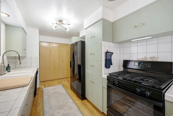 Full-size black range, tile backsplash, wood-finish flooring, and light green cabinetry