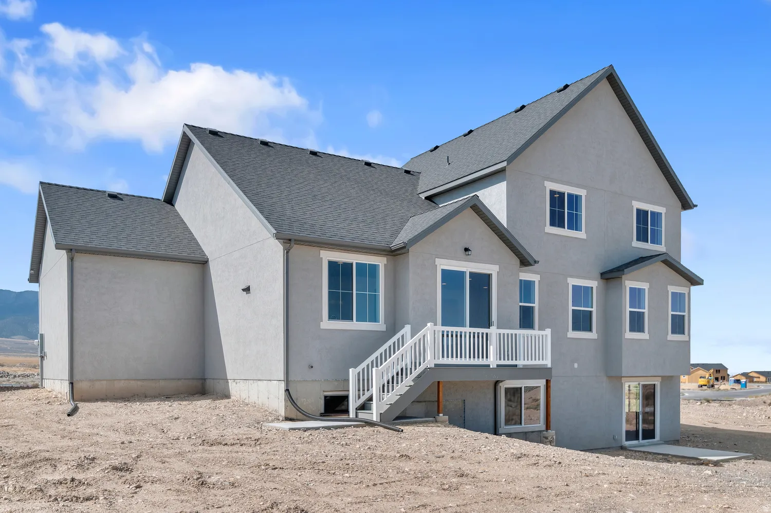 Exterior featuring light gray stucco, white-framed windows, dark gray shingle roofing, and a white deck with stairs