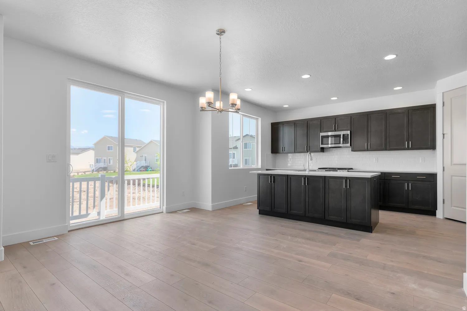 Open concept kitchen featuring dark wood cabinetry, white subway tile backsplash, stainless steel appliances, and a central island with a light-toned countertop