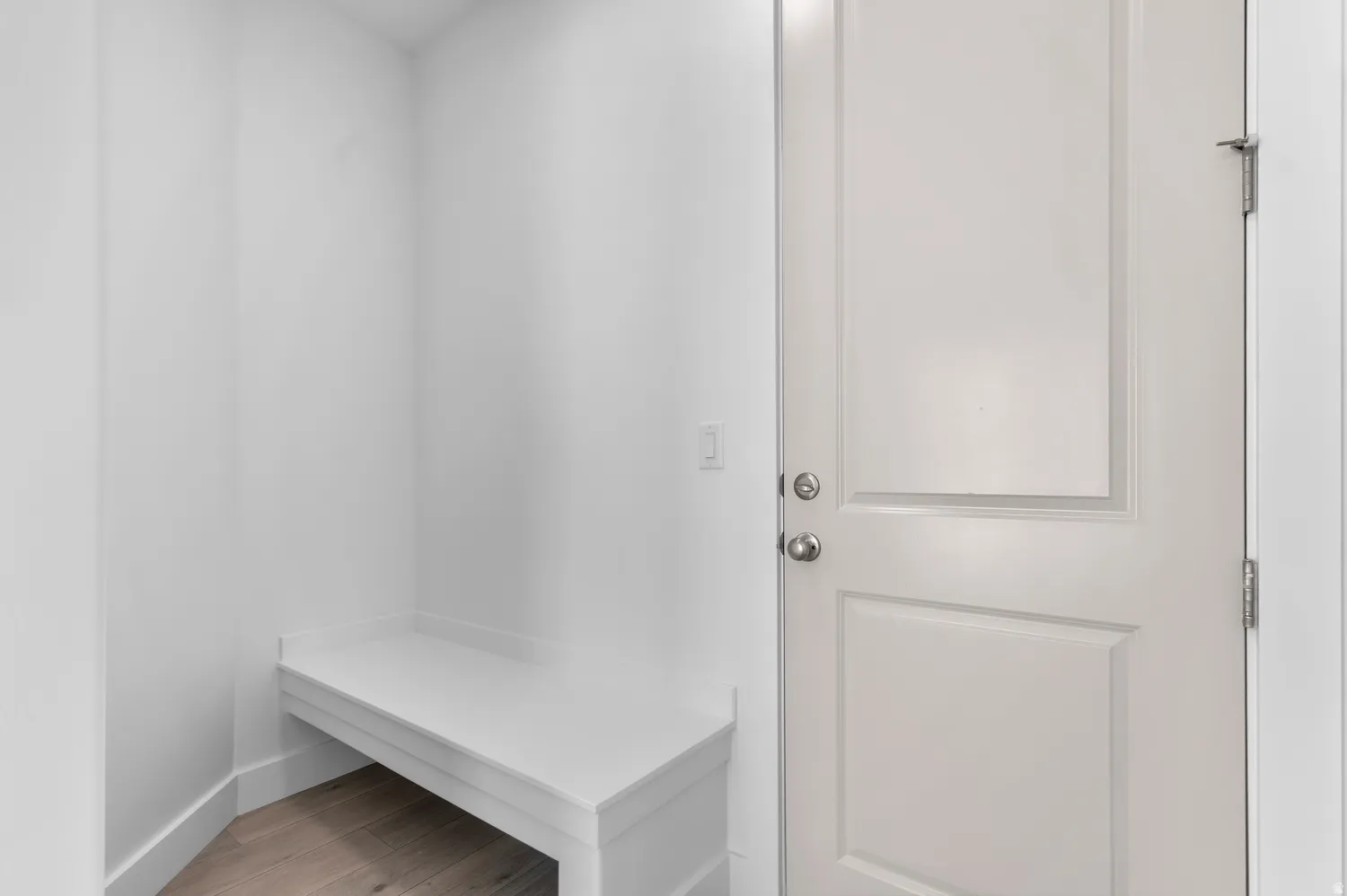 Built-in white bench seating, paneled door with satin nickel hardware, and wood-finish flooring