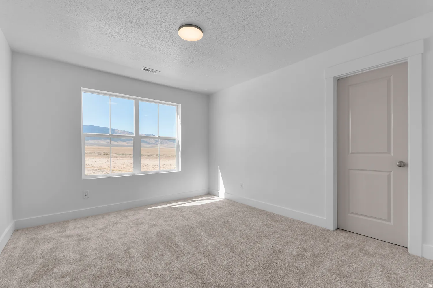 Neutral-toned carpeting, white walls, and a window with a distant mountain backdrop