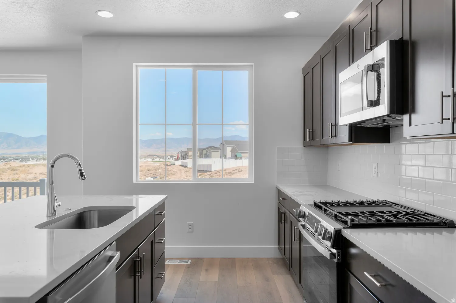 Kitchen featuring dark wood-finish cabinetry, light-toned countertops, subway tile backsplash, and stainless steel appliances