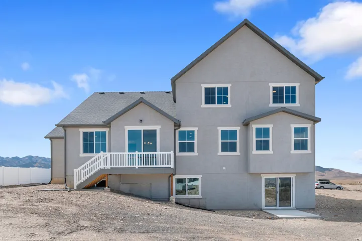 Stucco exterior with multiple windows, a second-story deck with white railings, and a walk-out basement featuring sliding glass doors