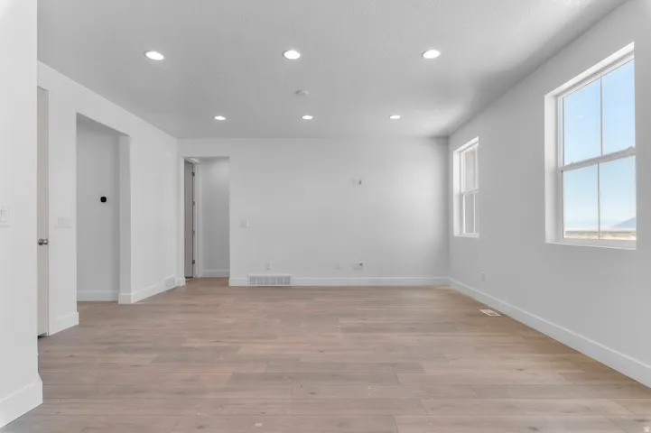 Recessed ceiling lighting, light wood-finish flooring, white walls, and multiple windows