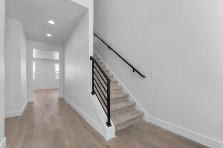 Hardwood-finish flooring, recessed ceiling lighting, carpeted staircase, and contemporary black metal railing