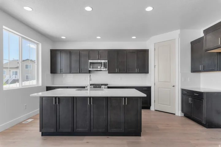 Kitchen featuring dark wood-finish cabinetry, a central island with a sink, stainless steel appliances, white countertops, and wood-finish flooring