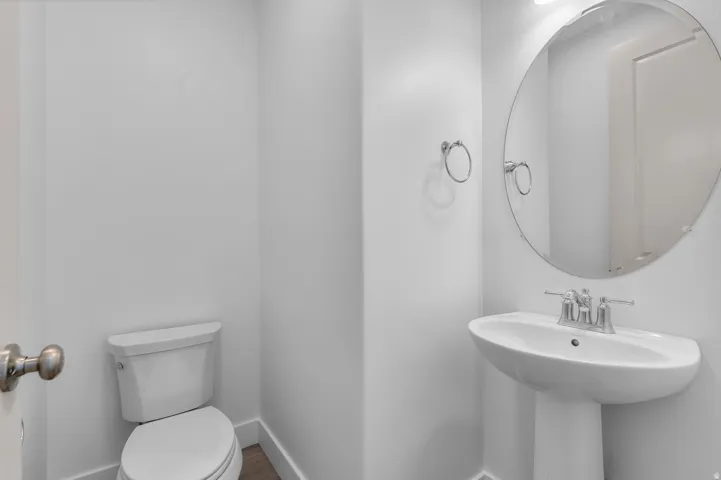 Pedestal sink with chrome faucet, circular frameless mirror, and wood-finish flooring