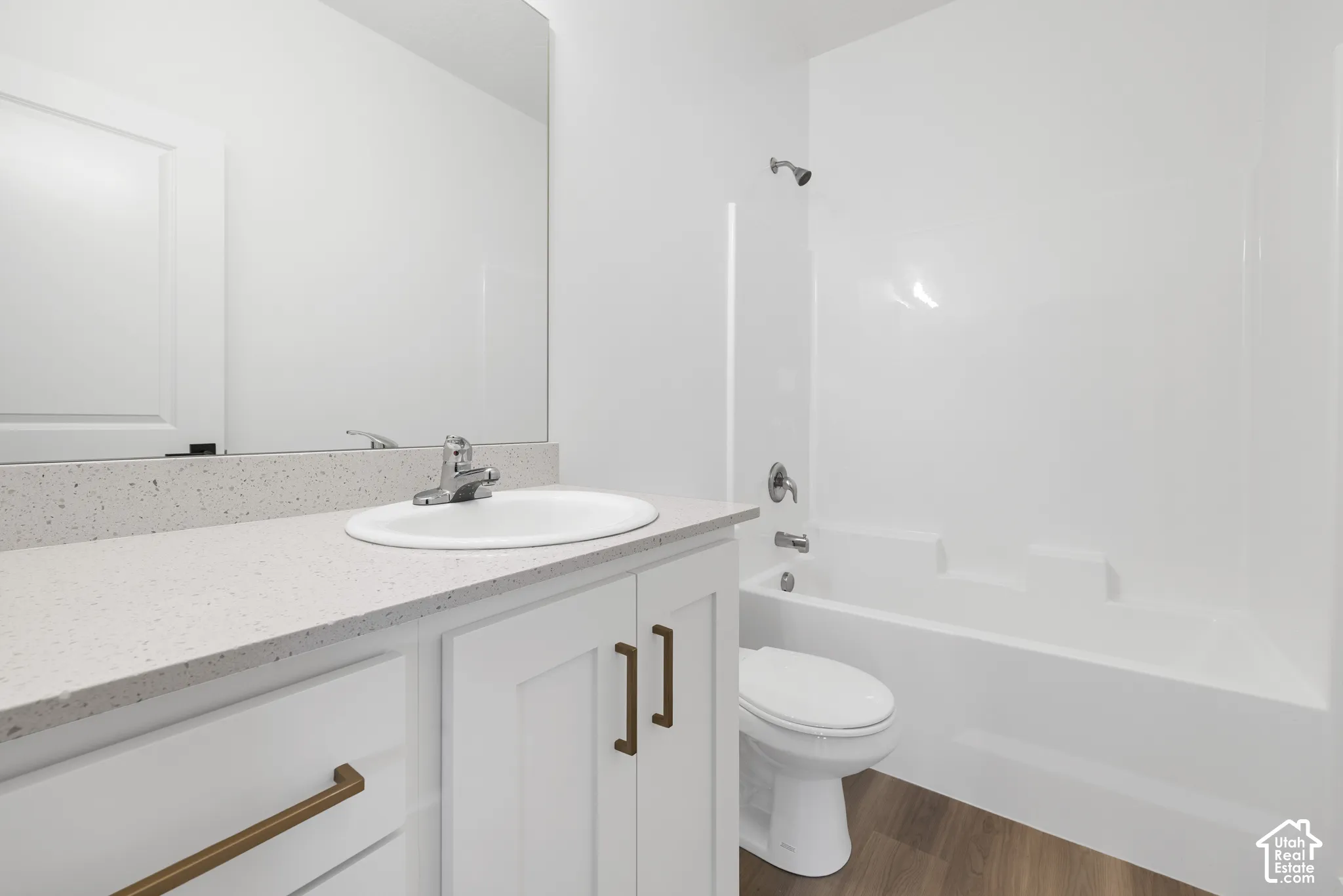 Bathroom featuring a white vanity with bronze hardware, a white undermount sink, a light-toned speckled countertop, and a white tub/shower combination