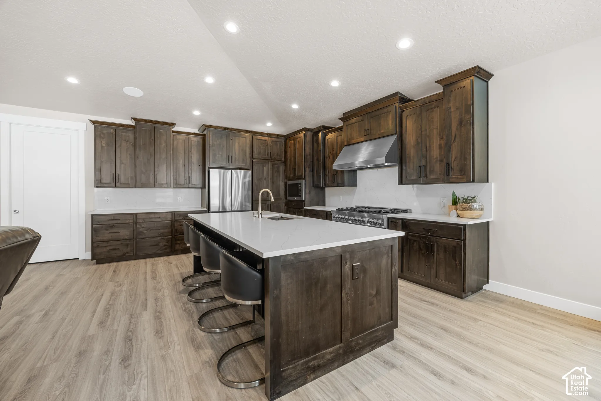 Kitchen featuring dark wood-finish cabinetry, light wood-finish flooring, a large center island with integrated seating, stainless steel appliances, and recessed lighting