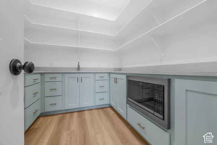 Corner pantry featuring extensive open shelving, light-toned wood-finish flooring, custom light blue cabinetry, and a built-in microwave