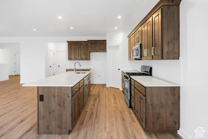 Kitchen featuring wood-finish flooring, white countertops, a stainless steel sink, a built-in microwave, and a gas range