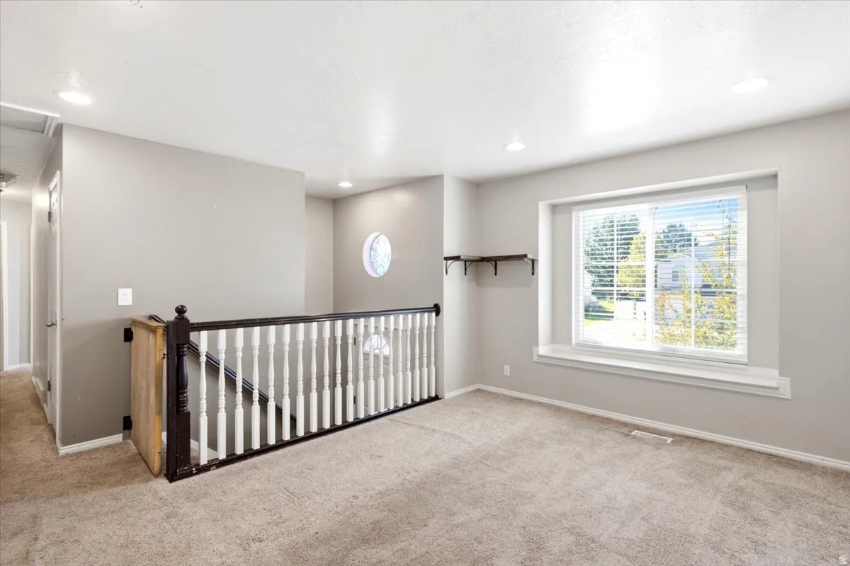 Carpeted landing featuring a white spindle railing, recessed lighting, a large window with blinds, and a round accent window