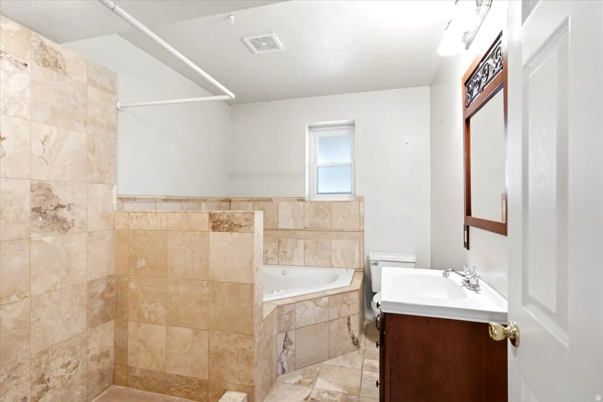 Tiled shower with a corner jetted tub, a single window, and a vanity with a white countertop