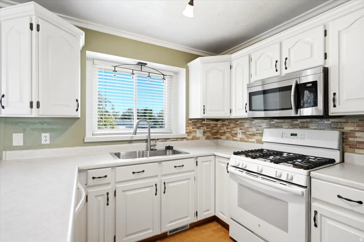 White cabinetry with dark hardware, stainless steel microwave, white range with gas cooktop, mosaic tile backsplash, and light-toned countertops