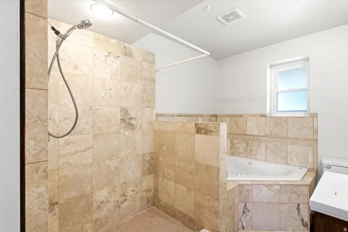 Tiled walk-in shower with a handheld shower head, corner soaking tub, and a single window