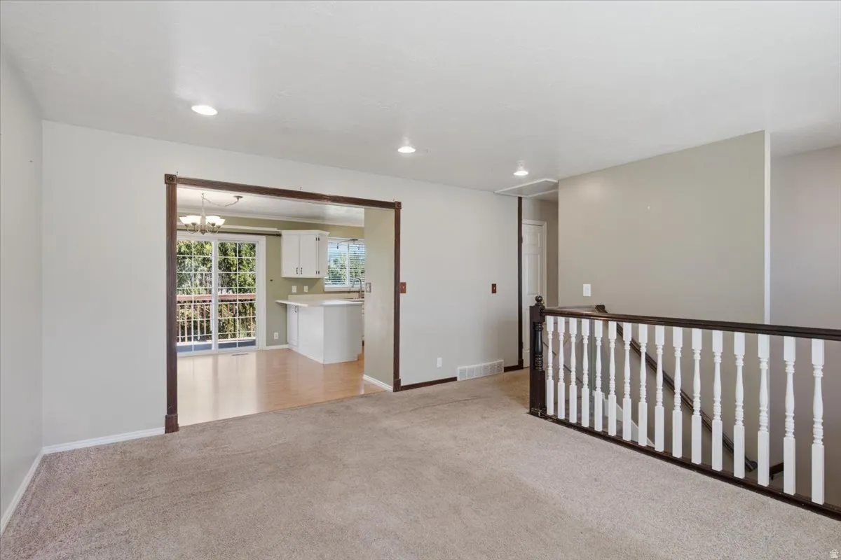Carpeted living area, staircase with wood-finish handrail and white balusters, recessed lighting, and a doorway with wood-finish trim