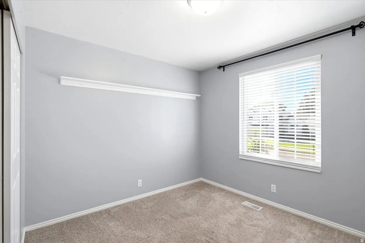 Neutral-toned walls with carpet flooring, a window with horizontal blinds, and a built-in wall shelf