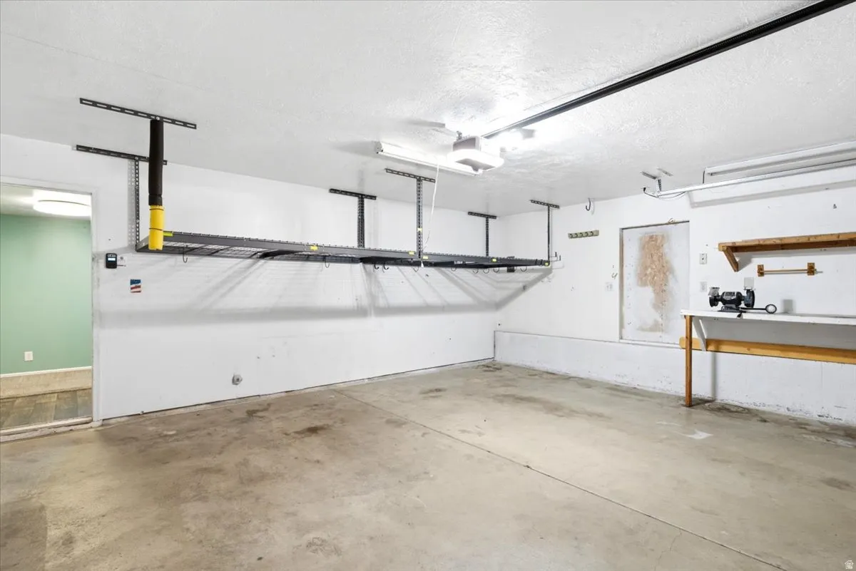Concrete flooring, ceiling-mounted storage racks, built-in shelving, workbench area, and overhead lighting