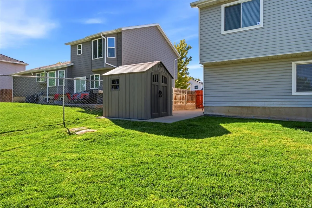 Expansive grassy yard with a chain-link fence, concrete patio, and a utility shed