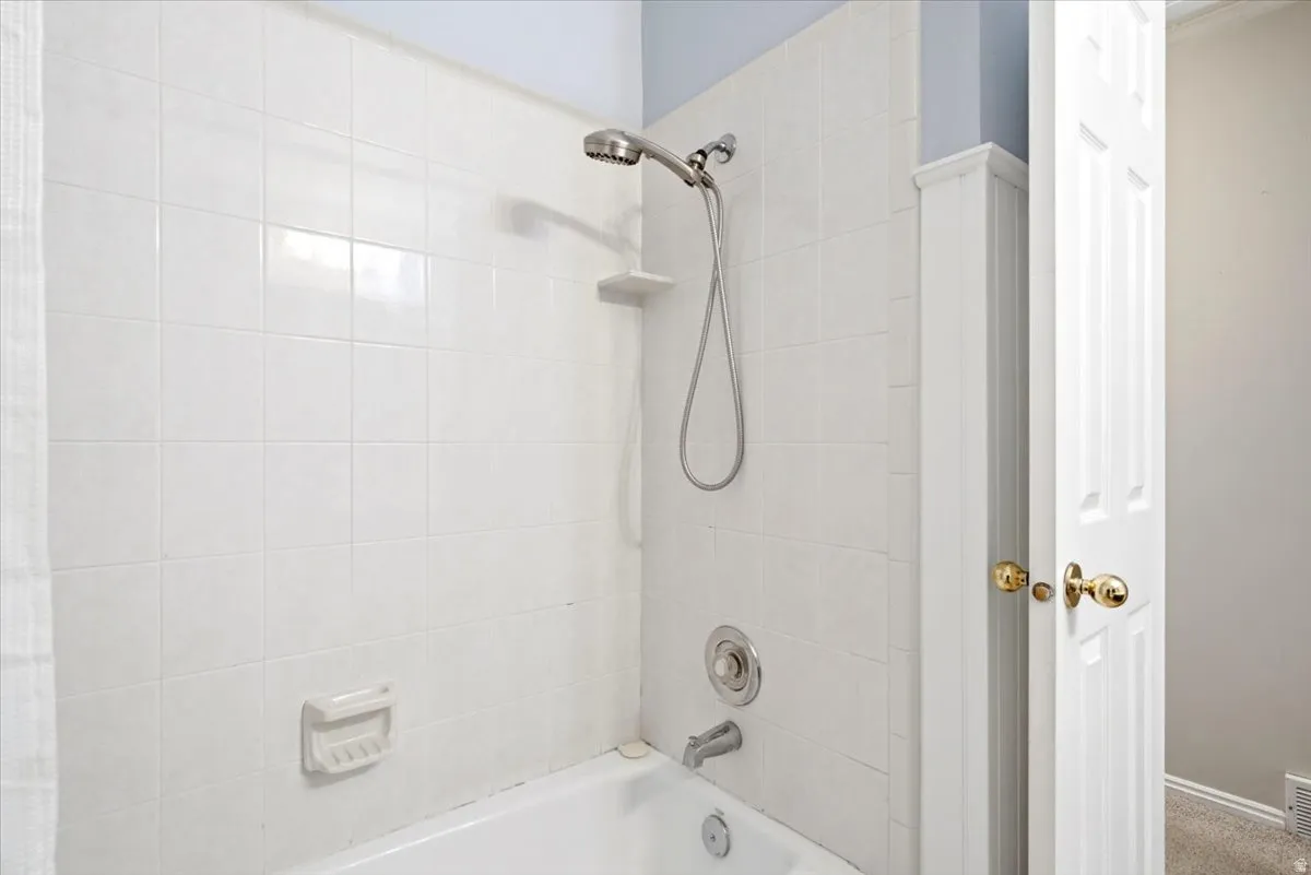 Bathtub with white tile surround, brushed nickel showerhead, and matching fixtures