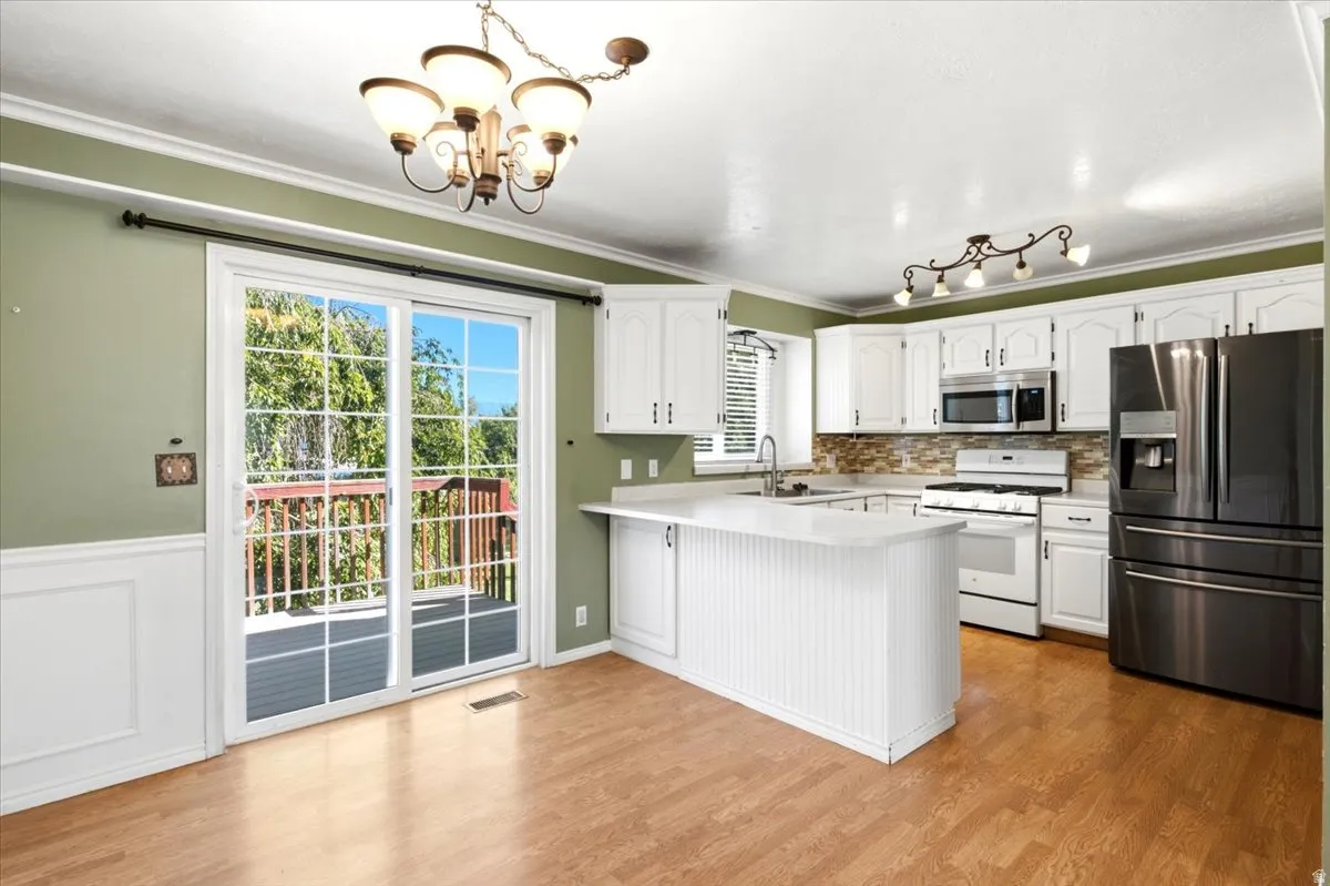 Kitchen featuring white cabinetry, light countertops, stainless steel appliances, wood-finish flooring, and a sliding glass door to an outdoor deck