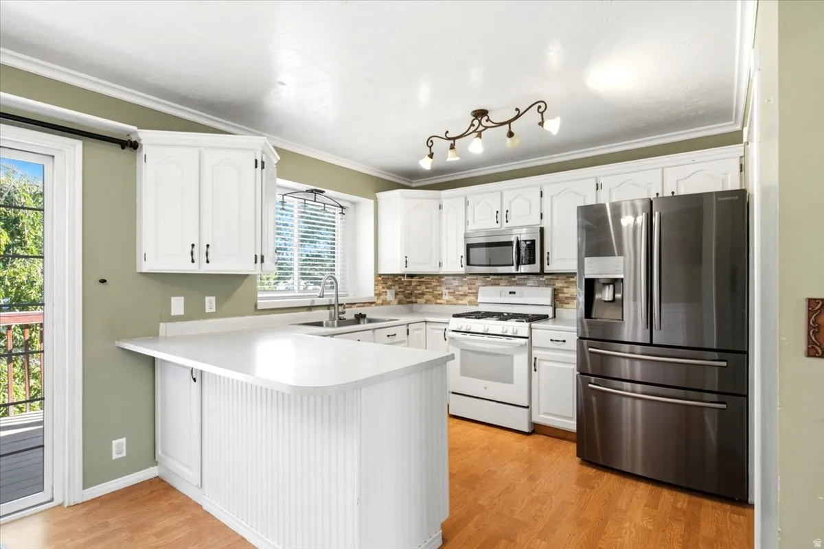 White cabinetry with dark hardware, stainless steel appliances, light-toned countertops, tile backsplash, and wood-finish flooring