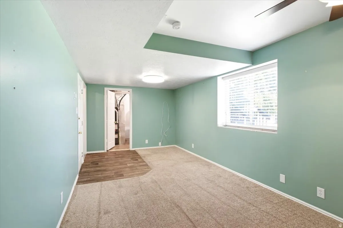 Room featuring a window with blinds, recessed ceiling detail, ceiling fan, and mixed flooring with carpet and wood-finish sections