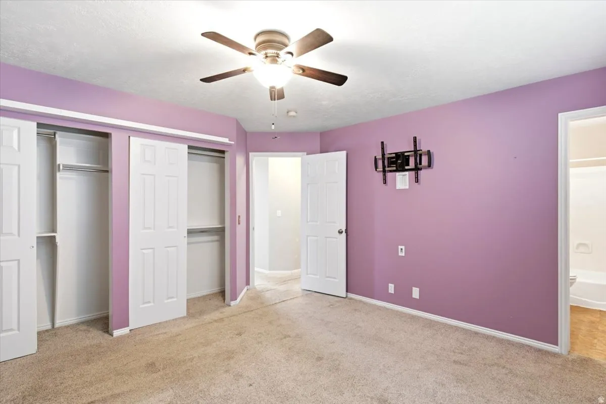 Plush carpet flooring, ceiling fan, white paneled doors, and dual sliding closet doors
