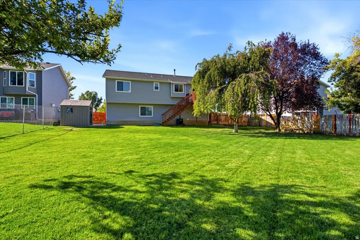Expansive backyard featuring a lush lawn, mature trees, a storage shed, and exterior stairs leading to the upper level