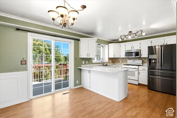 Kitchen featuring white cabinetry, light countertops, stainless steel appliances, wood-finish flooring, and a sliding glass door to an outdoor deck