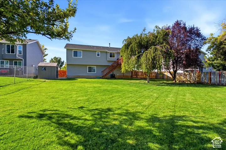 Expansive backyard featuring a lush lawn, mature trees, a storage shed, and exterior stairs leading to the upper level