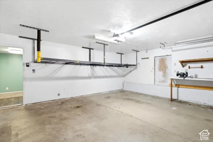 Concrete flooring, ceiling-mounted storage racks, built-in shelving, workbench area, and overhead lighting