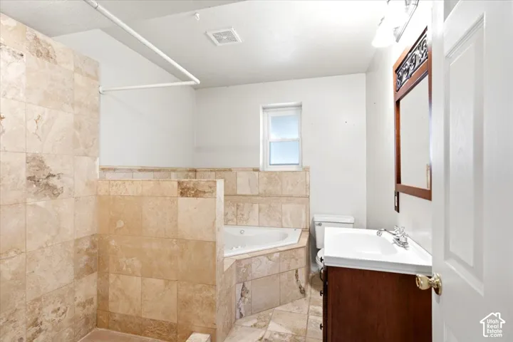 Tiled shower with a corner jetted tub, a single window, and a vanity with a white countertop