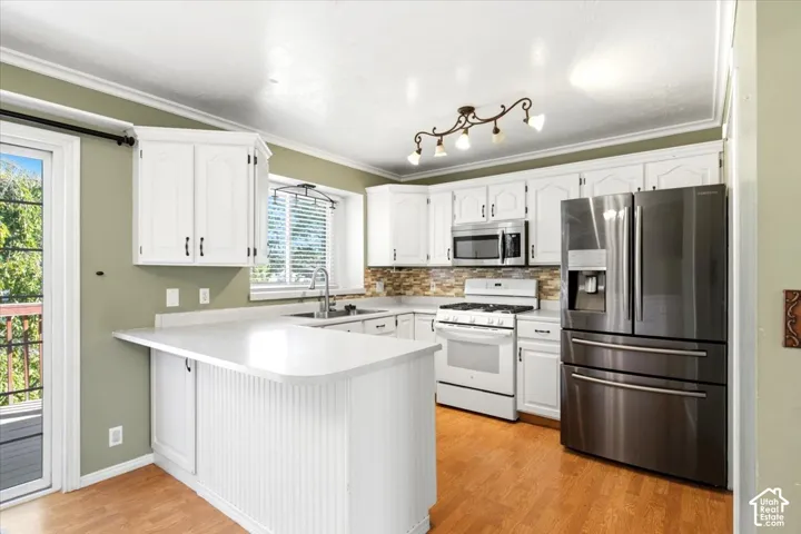 White cabinetry with dark hardware, stainless steel appliances, light-toned countertops, tile backsplash, and wood-finish flooring
