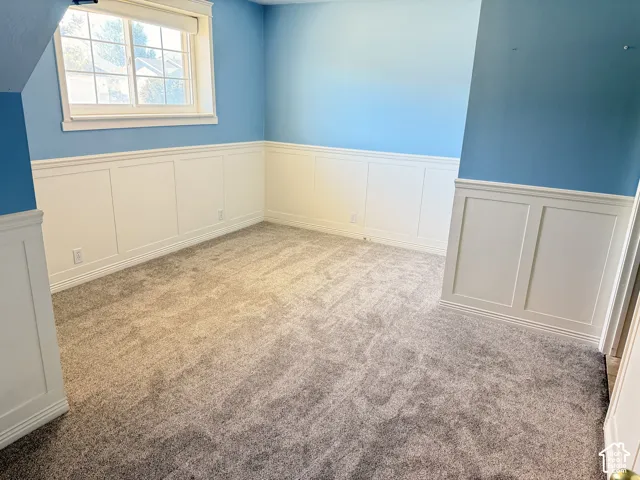 Wall paneling accents this room featuring window light and carpet flooring