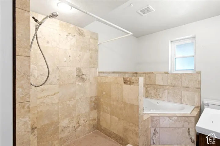 Tiled walk-in shower with a handheld shower head, corner soaking tub, and a single window