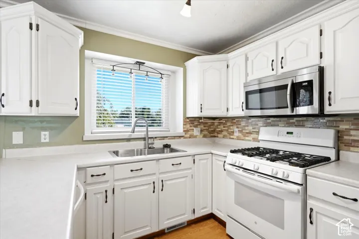 White cabinetry with dark hardware, stainless steel microwave, white range with gas cooktop, mosaic tile backsplash, and light-toned countertops