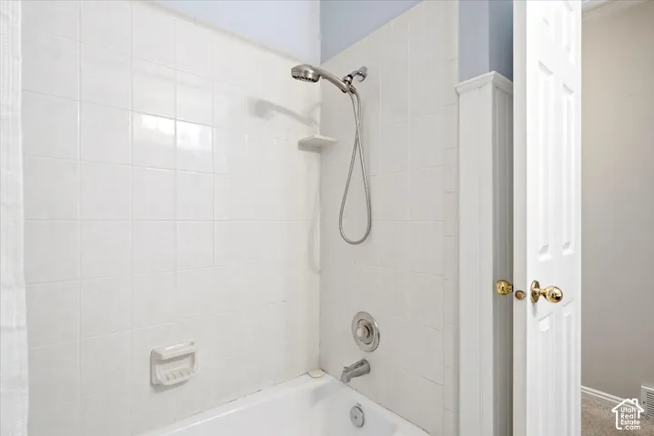 Bathtub with white tile surround, brushed nickel showerhead, and matching fixtures