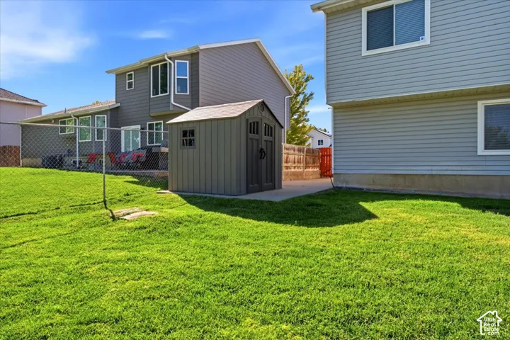 Expansive grassy yard with a chain-link fence, concrete patio, and a utility shed