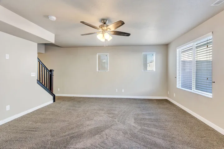 Carpeted flooring, ceiling fan, white window blinds, and staircase with dark wood newel post and balusters